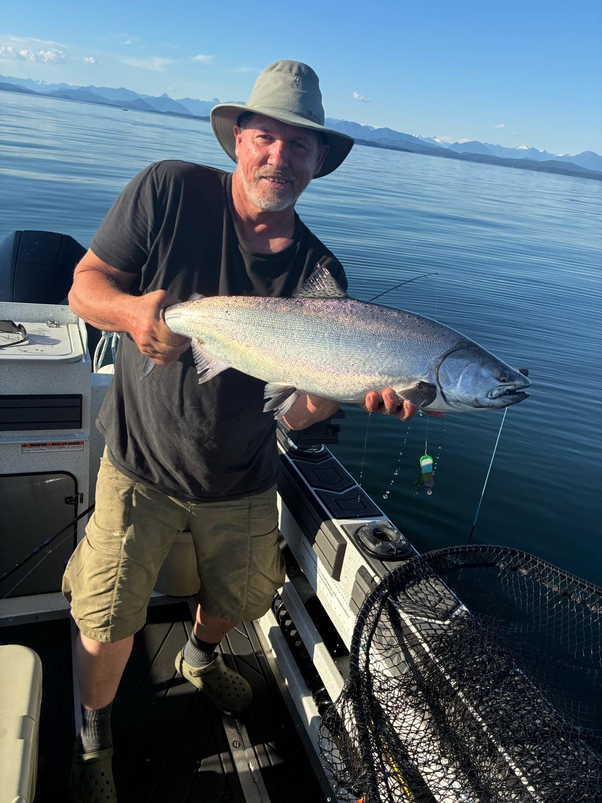 Angler holding bright silver salmon with BC mountains in background